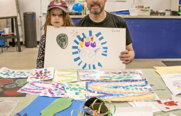 Parent and camper holding up artwork at a table