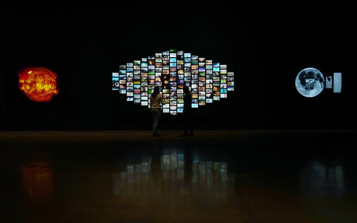 Two people standing in front of a digital video installation with 60 different videos
