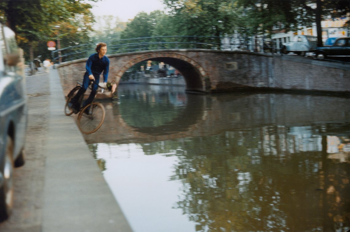 A video still from 16mm film of a man on a bicycle about to fall into a canal 