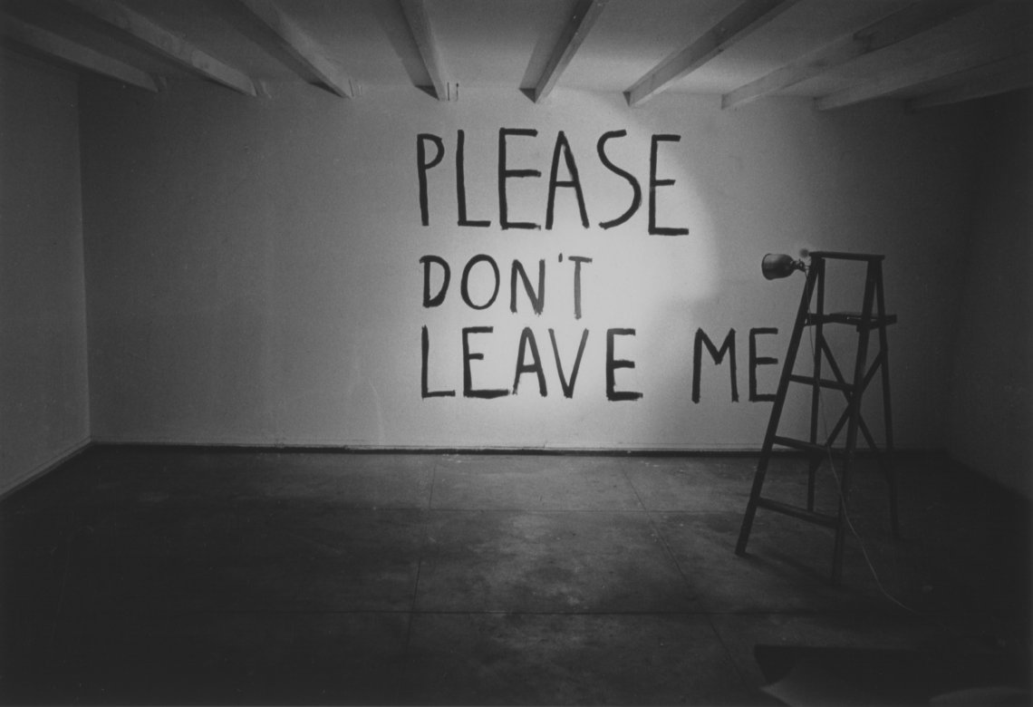 A black and white photograph of "Please Don't Leave Me" illuminated on the wall