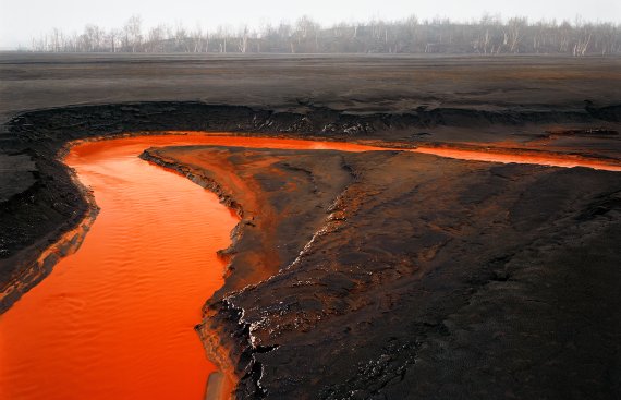 Aerial photo of vivid red nickel tailings in a river bed curling around barren-looking land