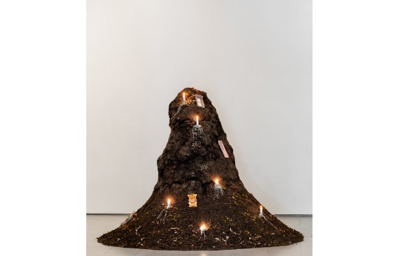 Mound of soil with lit candles spread throughout with a small fairy door on the top side