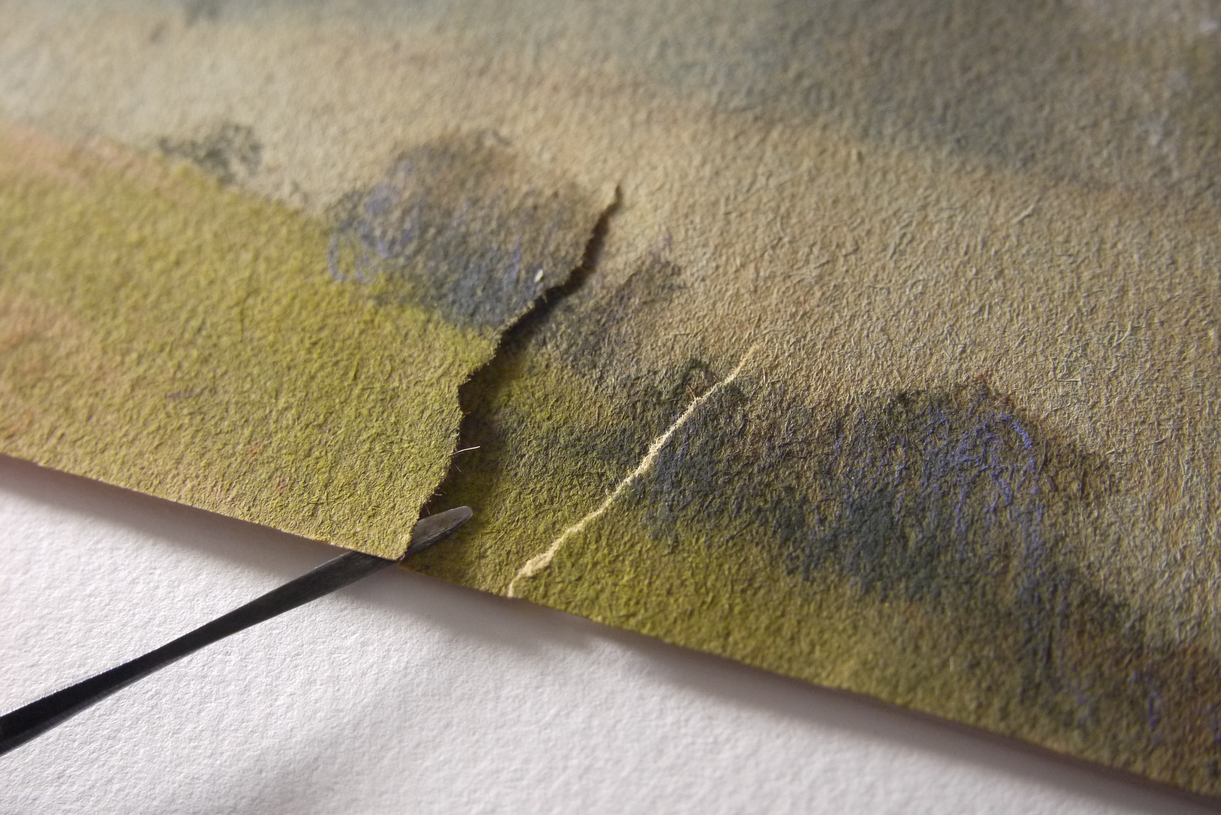 A close-up photo of a torn edge of the Cullen drawing, held slightly separated by a slender steel tool held by the conservator
