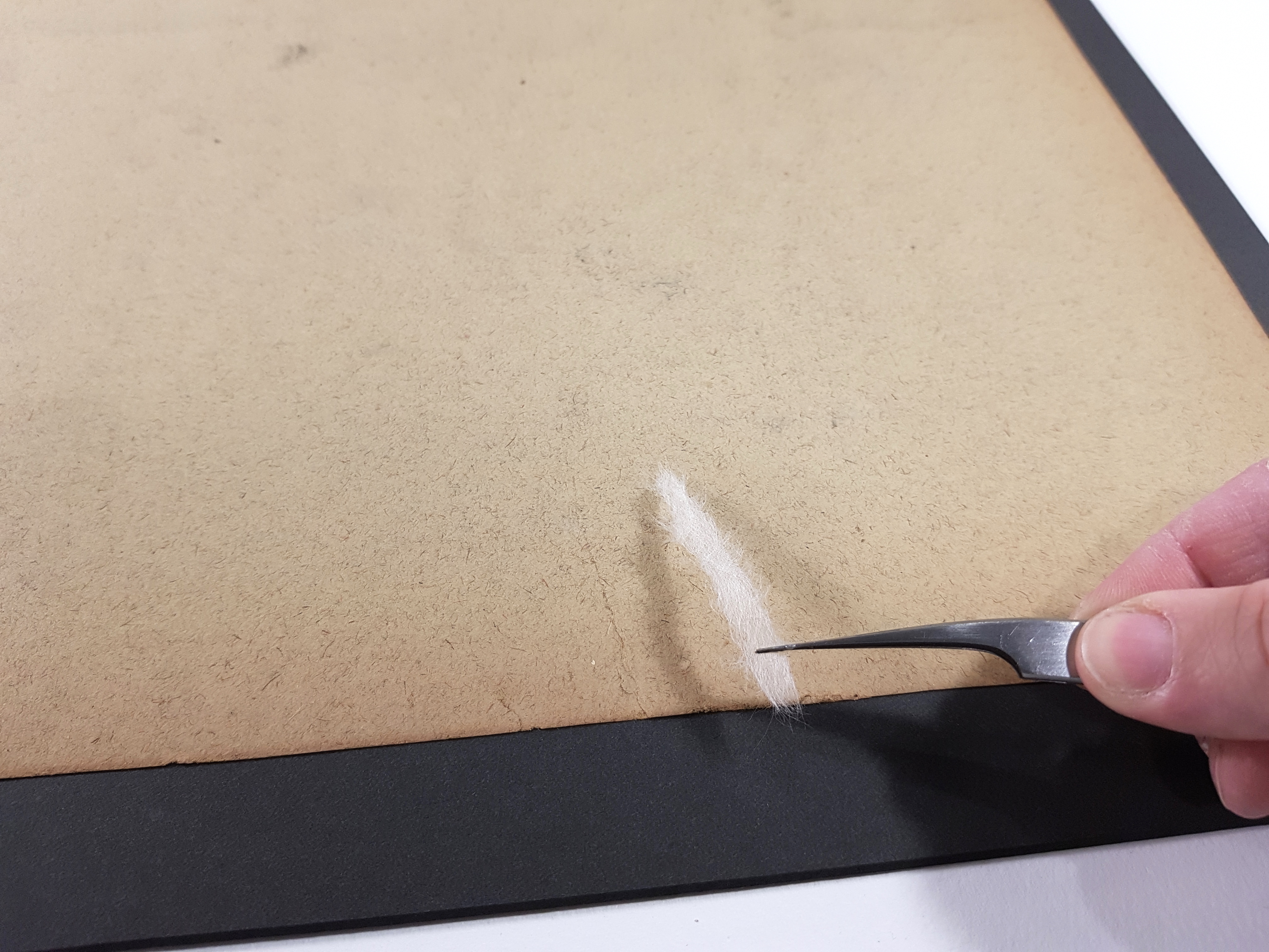 Detail photo of a thin piece of white Japanese paper being applied to the back of a tear in the drawing