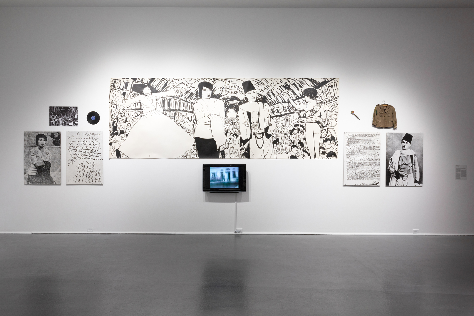 Installation view of The Oblivion Seekers, a multimedia installation of objects and small video arranged around a larger central black ink drawing