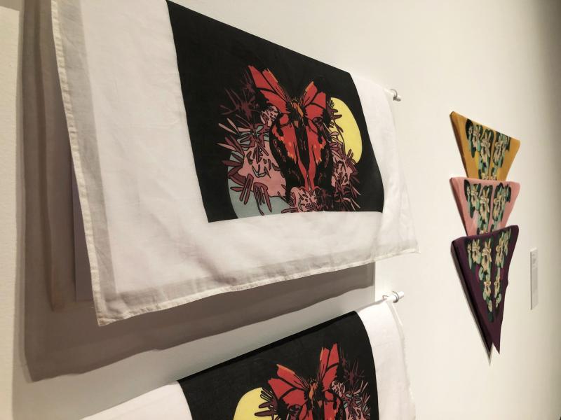 Close-up view of printed scarves hanging from a white rod next to an arrangement of three coloured kokum scarves