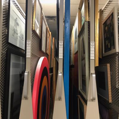 A sidelong view of painting racks with glimpses of paintings through the gaps between racks