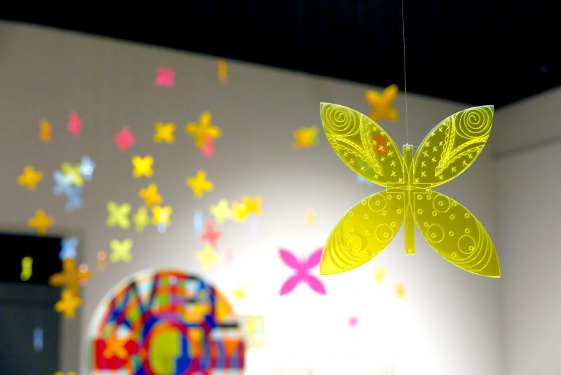 Detail view of laser-etched butterflies cut from neon plexiglass hanging in the middle of the gallery