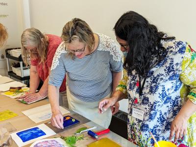 Three women at a studio table creating colourful monoprints