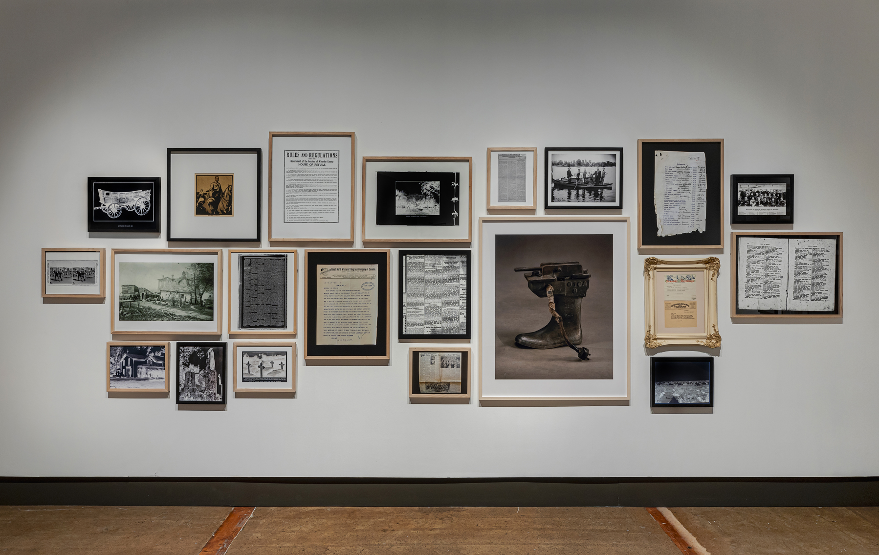 A salon-style arrangement of framed over twenty archival photos and documents on a white gallery wall